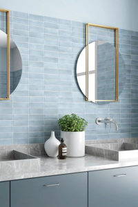 Pastel blauwe badkamer met licht blauwe keramische bejmat zelliges 5x15cm mat horizontaal recht op recht geplaatst aan de badkamer muur in combinatie met een grijs marmer wasbak en gouden spiegels