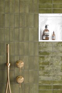 Aan deze douche muur werden mos groene wandtegels bejmat 5x15cm mat en blinkend gecombineerd. De douche werd afgewerkt met een wit marmer nis en gouden kranen.